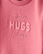 Sudadera rosa con mensaje “More Hugs Please”
